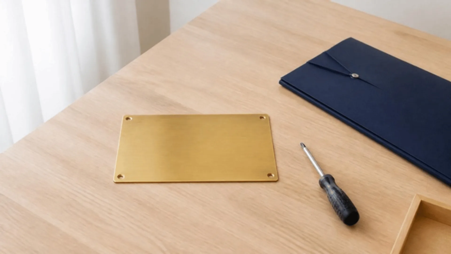 Plaque de porte en laiton vierge posée sur un bureau à côté d'un tournevis et d'une chemise fermée