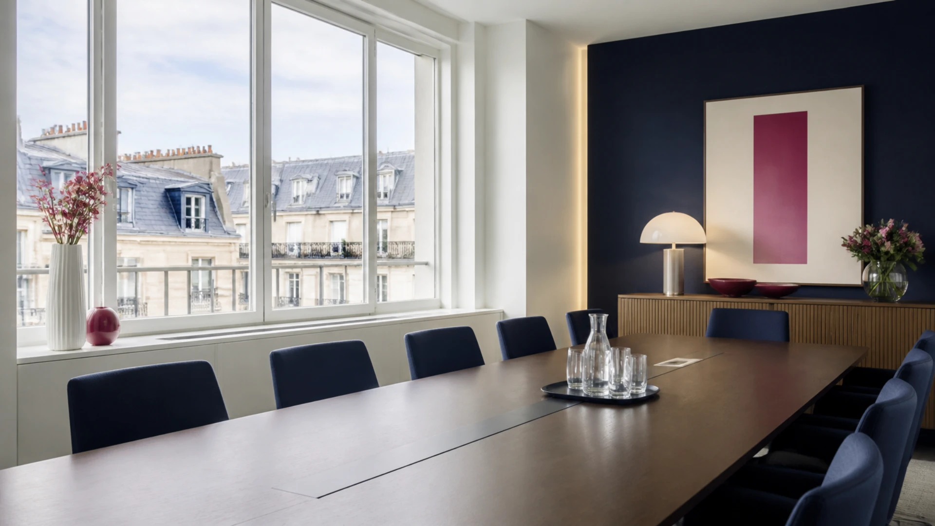 Longue table de salle de conseil avec chaises vides devant une fenêtre donnant sur des toits