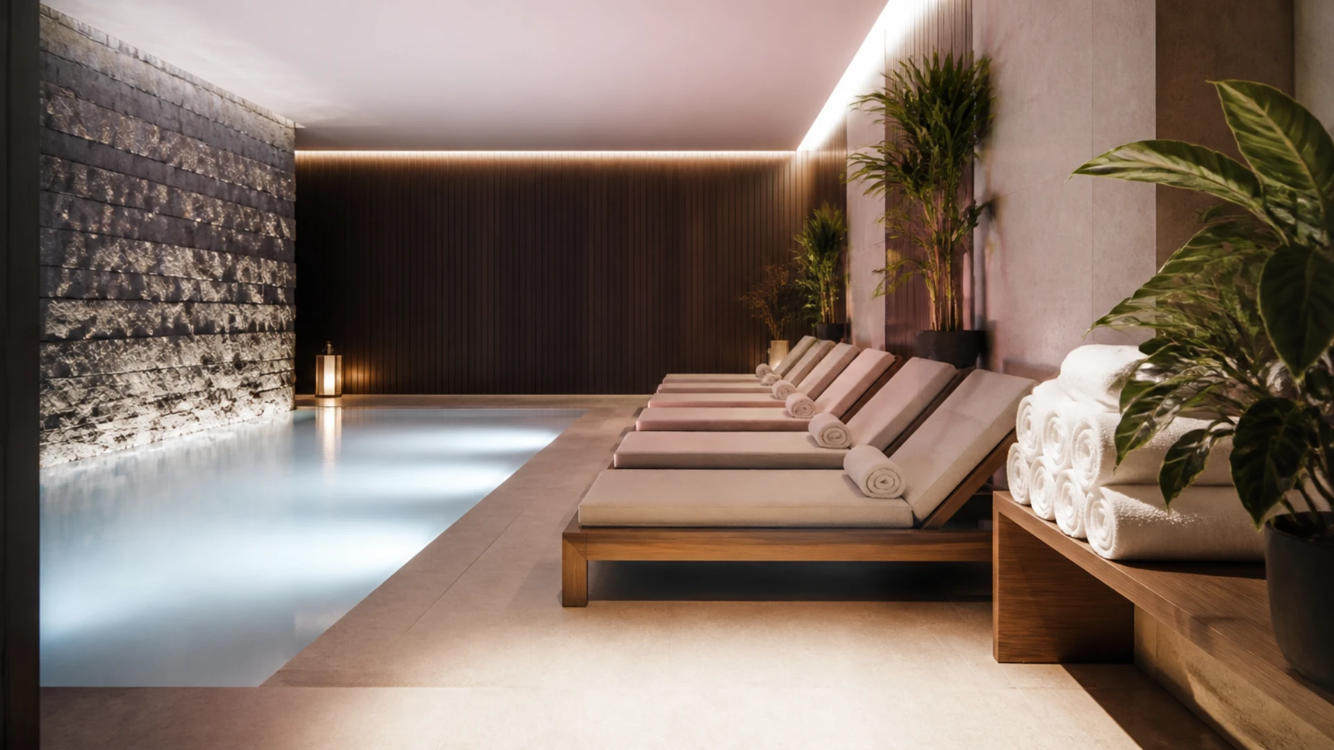 Espace détente d’un spa avec bassin éclairé, transats en bois et serviettes roulées