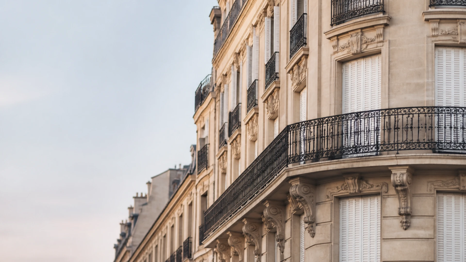 Immeuble d’habitation haussmannien vu depuis le trottoir, volets fermés à plusieurs étages
