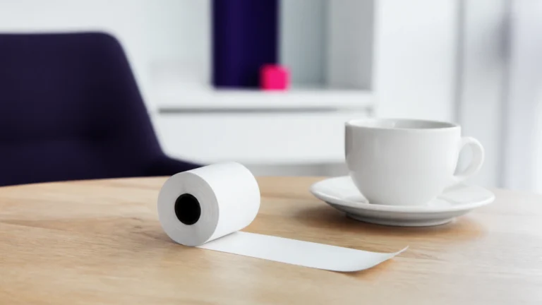 Rouleau de papier thermique vierge partiellement déroulé posé près d'une tasse vide