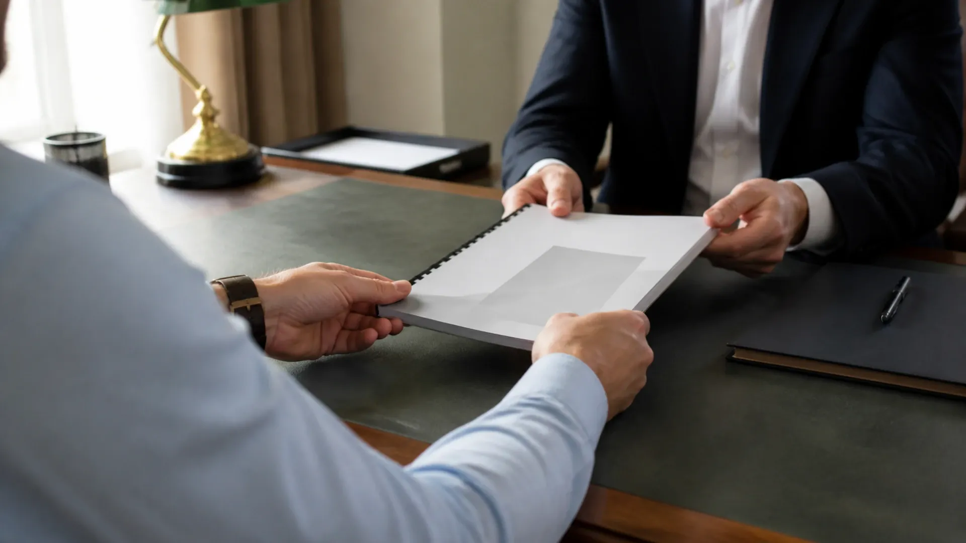 Un entrepreneur tend un dossier relié à son interlocuteur de l’autre côté d’un bureau, visages hors cadre